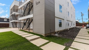 A modern multi-story building with a grey facade, a visible staircase, and a well-maintained lawn. - Modern Stylish Oasis in Downtown Dallas w Parking (Dallas)