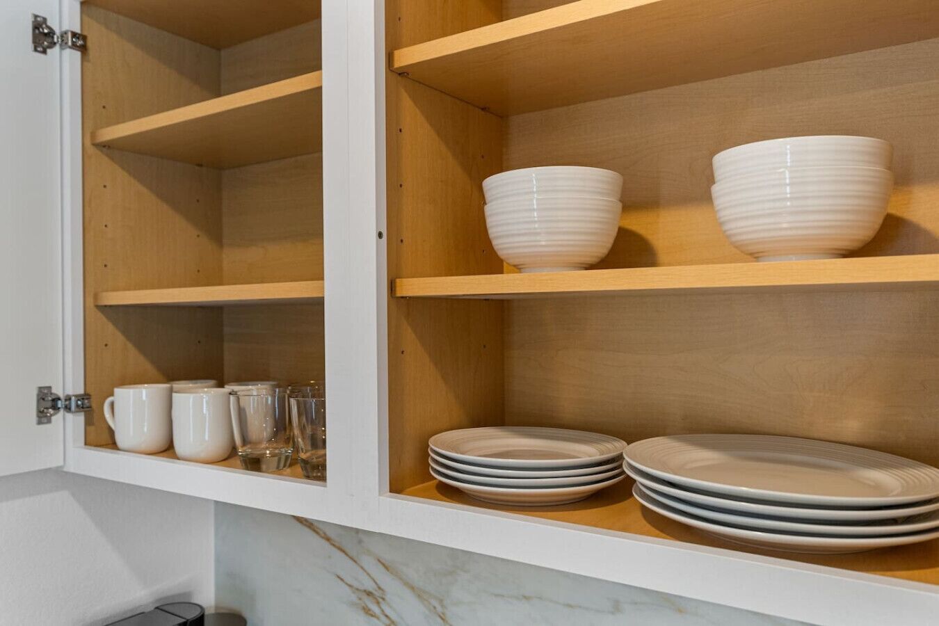 A kitchen cabinet with shelves holding white bowls and plates.
