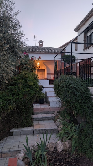 A courtyard with stone steps leading to a building entrance, surrounded by greenery and a tiled roof.