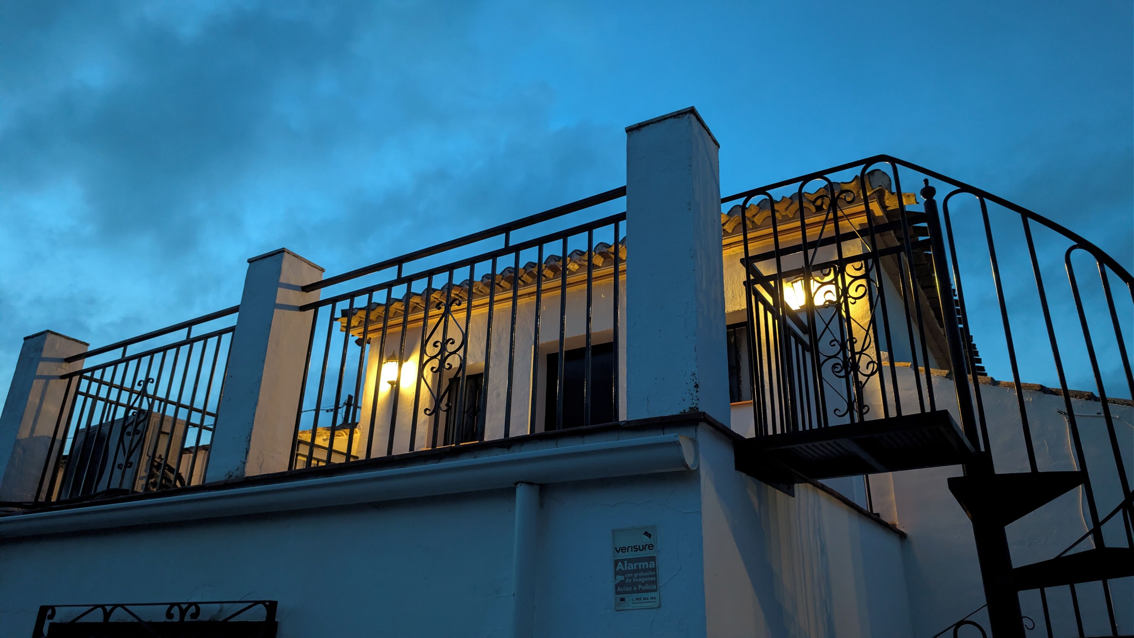 Un bâtiment doté d’un balcon, d’un escalier et d’une enseigne indiquant la présence d’un système d’alarme de sécurité.