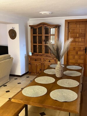 Una mesa de comedor con individuales tejidos, un jarrón de fibras naturales con plantas secas, un mueble de madera y una puerta con un diseño geométrico.