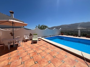 A rooftop pool area with a clear view of the mountains, a tiled patio, and outdoor furniture.