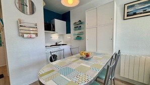 A dining area with a round table, chairs, a clock, and a kitchen in the background. - Quiberon - 2rooms - 27m² - beach (QUIBERON)