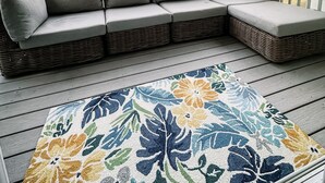 Een overdekt terras met een hoekbank en een decoratief vloerkleed.