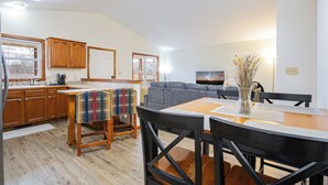 Una cocina amplia con armarios de madera, una zona de comedor con mesa y sillas, y un sofá gris en la sala de estar.