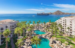Un resort con piscina, palme e vista sull'oceano e su una nave da crociera.