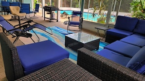 A covered outdoor seating area with blue cushioned chairs and a wicker sofa, a grill, and a pool in the background. - Free Huge Heated Pool, Spacious, Comfy Beachy Vibes! (Largo)