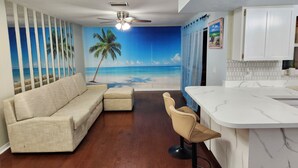 A living room with a beach mural, a sofa, a bar area, and a ceiling fan. - Free Huge Heated Pool, Spacious, Comfy Beachy Vibes! (Largo)