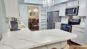 A modern kitchen with a large island, white cabinetry, stainless steel appliances, and a chandelier. - Free Huge Heated Pool, Spacious, Comfy Beachy Vibes! (Largo)