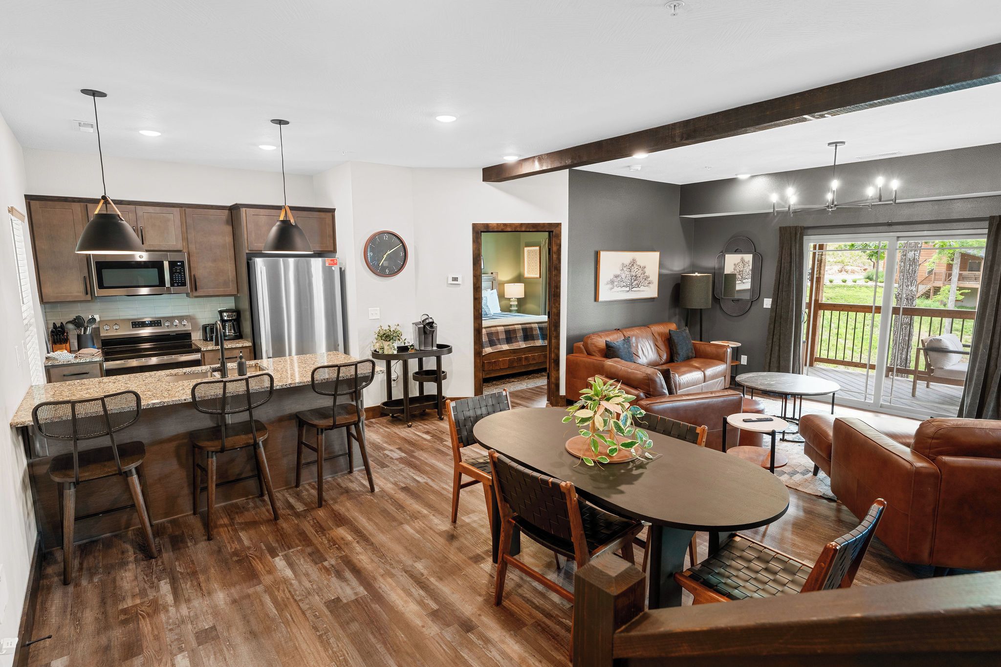 A modern kitchen with stainless steel appliances, a dining area with a round table and chairs, and a living room with a leather sofa and a view of the outdoors.