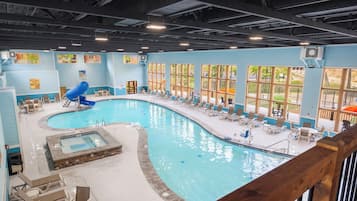 A large indoor swimming pool with a hot tub, lounge chairs, and large windows.
