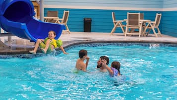 A pool area with a blue slide, lounge chairs, and a tiled pool edge.