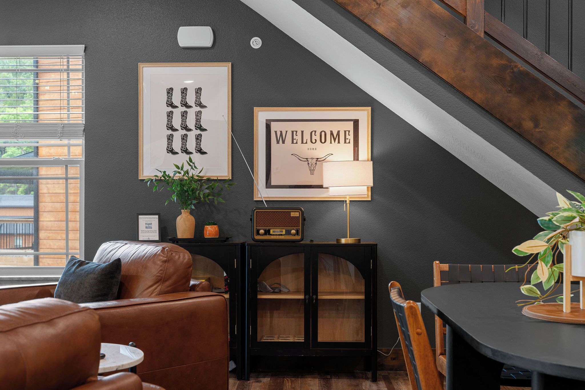 A cozy living room with a leather couch, a dining table, a radio, and framed artwork on the wall.