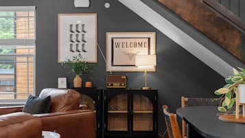 A cozy living room with a leather couch, a dining table, a radio, and framed artwork on the wall.