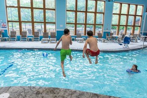 Une piscine intérieure à l’eau d’un bleu limpide, dotée de chaises longues en bois et de grandes fenêtres.