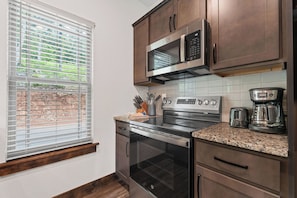 A kitchen with a stainless steel range, a microwave, a coffee maker, and a window with blinds.