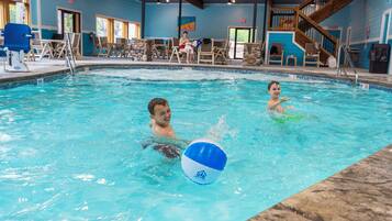 Ein Hallenschwimmbad mit klarem Wasser, einem Rettungsschwimmerstuhl und einem blau-weißen Ball.