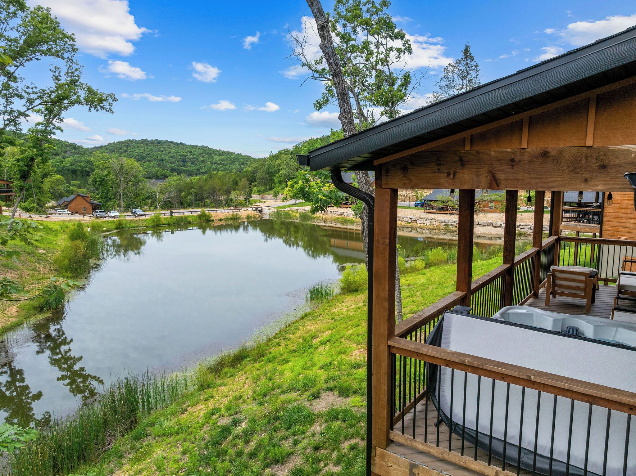 A wooden deck with a hot tub, overlooking a calm lake with a forested hill in the background.