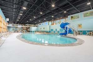 Une piscine intérieure dotée d’un toboggan bleu, de plusieurs couloirs de nage et d’un espace abrité avec des sièges.