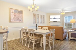 A dining area with a white table and chairs, a sofa, and a television on the wall. - Lake Access Condo with Expansive Deck Area, Community Pool & Free Attraction Tickets (Kimberling City)