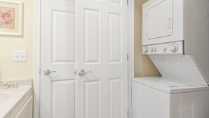 Uma lavanderia com máquina de lavar e secadora frontais, uma porta branca e um interruptor de luz fixado na parede.