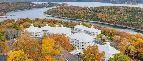 A large building with multiple wings, surrounded by autumn foliage and a body of water.