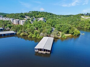 A lakeside property with a dock extending into the water, surrounded by dense greenery and residential buildings.