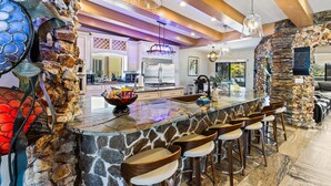 Una cocina moderna con una isla de piedra, taburetes de bar e iluminación colgante.