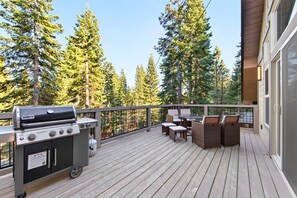 A wooden deck with a grill, outdoor furniture, and a view of tall trees.