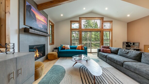 A spacious living room with a fireplace, a blue sofa, a grey sofa, and a glass coffee table.