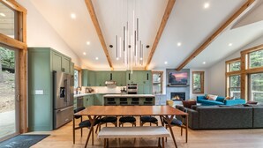 A modern kitchen with a dining area, wooden beams, and large windows.