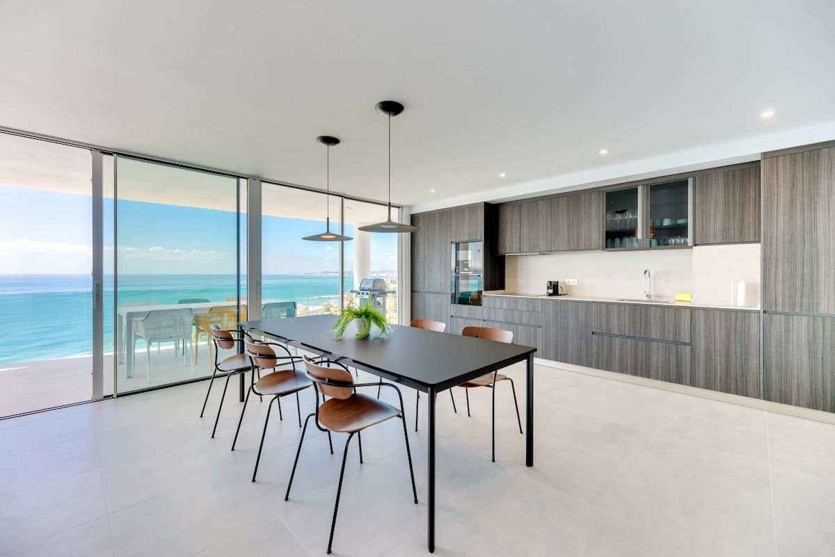 Een moderne keuken met een grote eettafel, stoelen en uitzicht op de oceaan.
