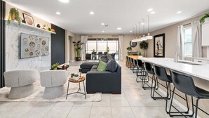 A modern kitchen with a dining area, featuring a marble backsplash, black chairs, and a white countertop. - Stylish Orlando Resort Home w Private Pool (Kissimmee)