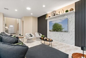 Ein modernes Wohnzimmer mit einer Couch, Sesseln, einem Couchtisch und einem an einer Marmorwand montierten Fernseher.