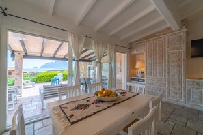 A dining area with a table set for two, a bowl of fruit, and a view of the outdoors.