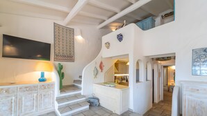 A staircase with a white wall, a flat-screen TV, a cactus, and a small kitchen area.