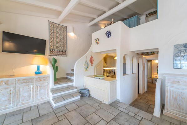 A staircase with a white wall, a flat-screen TV, a cactus, and a small kitchen area.