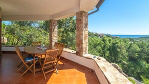 A covered outdoor dining area with a table and chairs, stone pillars, and a view of a lush landscape and coastline. - Villa 'Vista Mare Cala Ginepro' with Sea View, Private Terrace and Air Conditioning (Punta Molara)