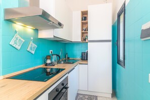 Uma cozinha compacta com um fogão por indução preto, uma coifa de aço inoxidável e um forno embutido.