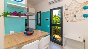 A modern kitchen with a wooden table, white chairs, a blue and white backsplash, and a view through an open door to an outdoor area. - Villa 'Vista Mare Cala Ginepro' with Sea View, Private Terrace and Air Conditioning (Punta Molara)