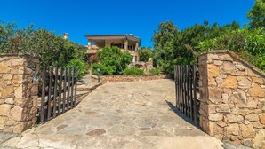 A stone pathway leading to a house with a stone wall on one side and a metal gate on the other. - Villa 'Vista Mare Cala Ginepro' with Sea View, Private Terrace and Air Conditioning (Punta Molara)
