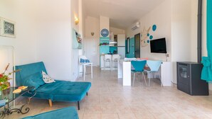 A modern living room with a sofa, a dining area with chairs, a kitchen in the background, and a TV mounted on the wall. - Villa 'Vista Mare Cala Ginepro' with Sea View, Private Terrace and Air Conditioning (Punta Molara)