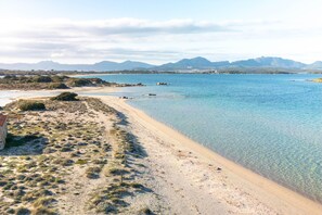 Una playa con aguas cristalinas, una orilla arenosa y montañas a lo lejos.