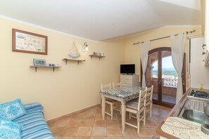 A cozy room with a dining table, chairs, a TV, and a balcony with curtains.