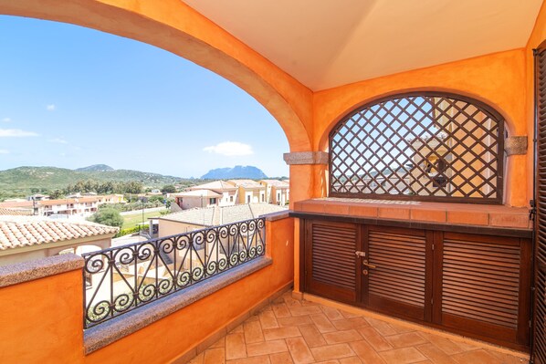 A balcony with a view of a residential area, a metal gate, and a tiled floor.