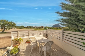 An outdoor seating area with a table and chairs, surrounded by a white fence, overlooking a landscape with trees and a distant mountain.