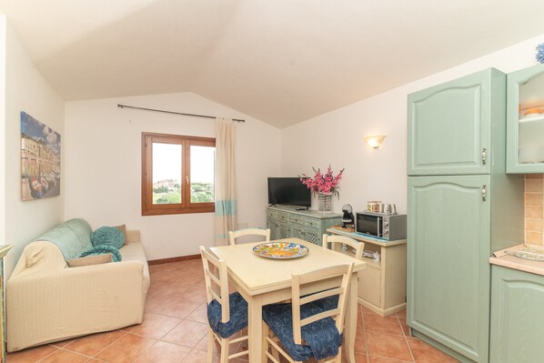 A compact living space with a dining table, chairs, a sofa, a television, and a kitchen area.