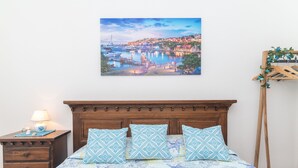Une chambre à coucher avec un lit, une tête de lit en bois, une table de chevet, une lampe et un tableau représentant une ville côtière.