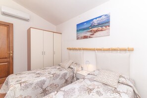A bedroom with two beds, a wardrobe, a painting of a beach scene, and a mounted air conditioner.