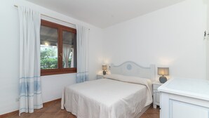Ein Schlafzimmer mit einem Bett, zwei Nachttischen mit Lampen, einem Fenster mit Vorhängen und einem weißen Schrank.